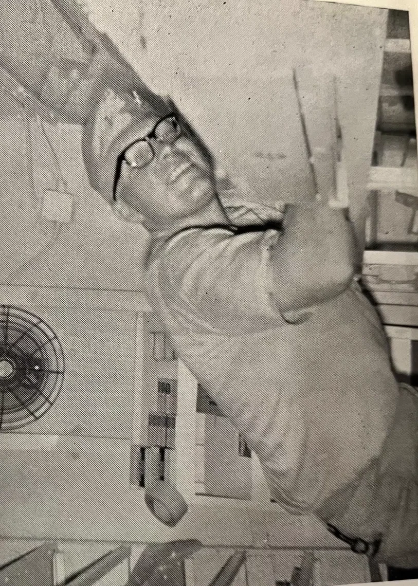 Lewis Wiens during his Navy service, smiling in a cap and glasses inside a ship’s compartment